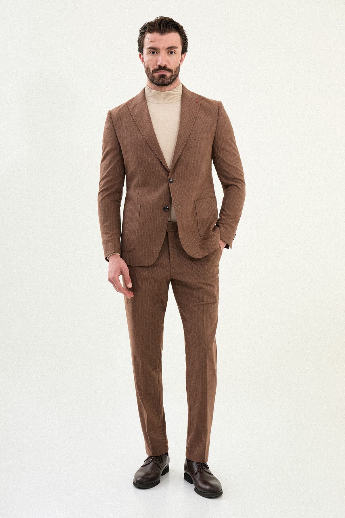 Men’s camel slim-fit mono-collar suit with pointed minimalist collar, matte micro-texture fabric, single-breasted jacket, and styled with a cream turtleneck for tonal winter dressing.